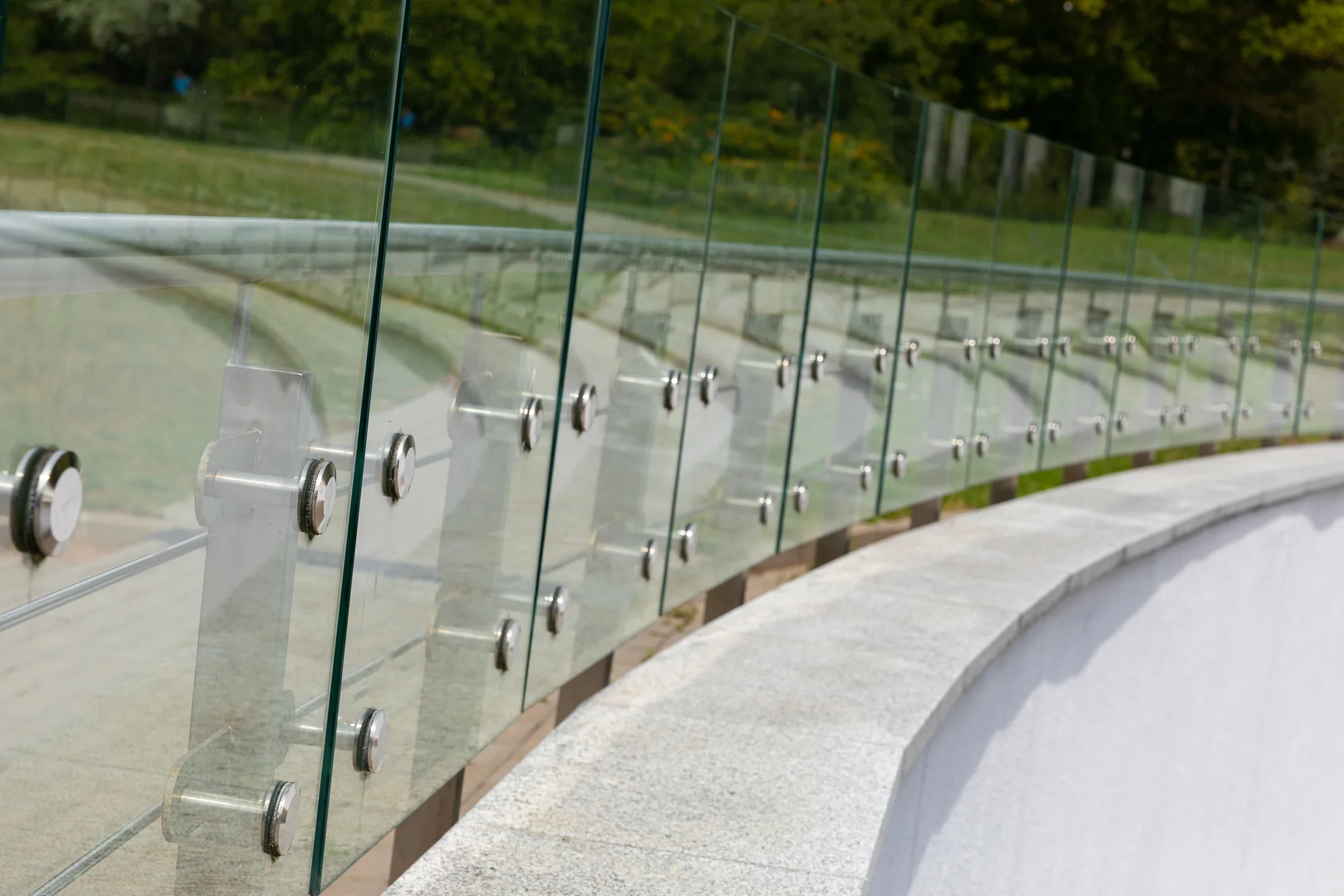 A curved glass balustrade with stainless steel fittings along a commercial walkway
