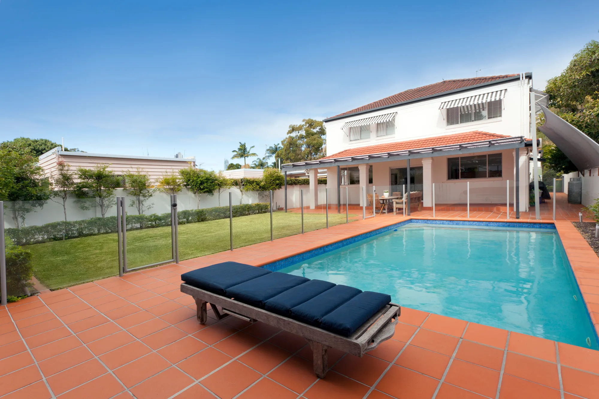 Frameless glass pool fence around a backyard pool with brick paving in Brisbane